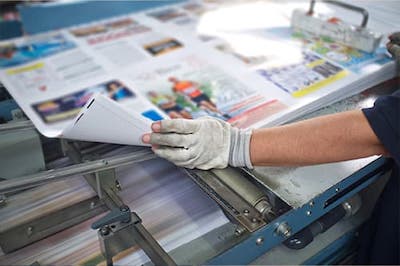 person standing at printing machine with large size paper of images and content