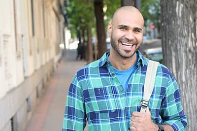 smiling man with backpack standing on a sidewalk next to a building