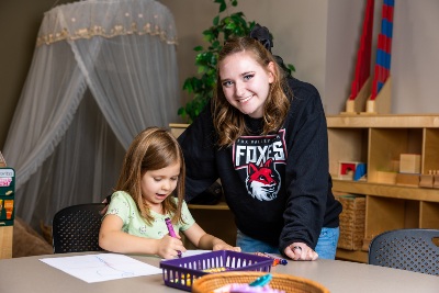 child care teacher with toddler coloring at a table