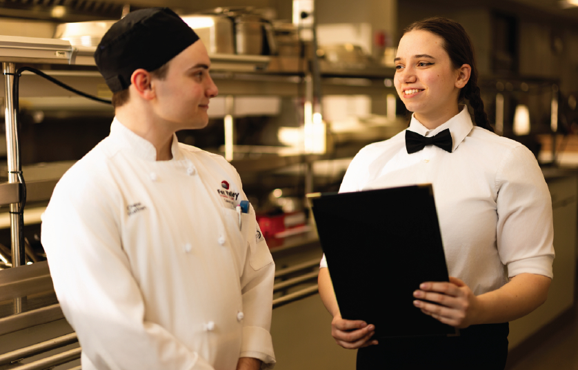 Culinary student holding menu smiling at another culinary student