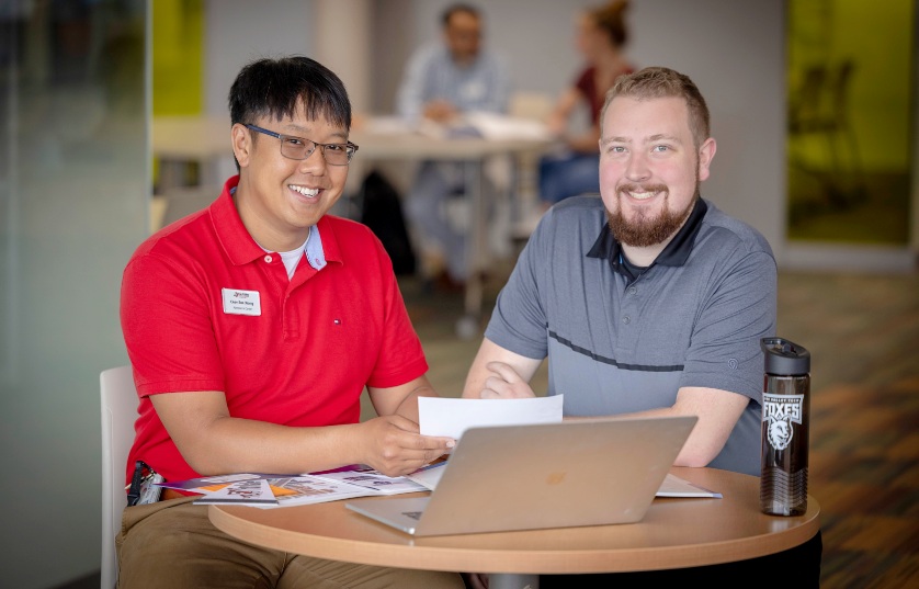 student and teacher working at a table smiling at the camera
