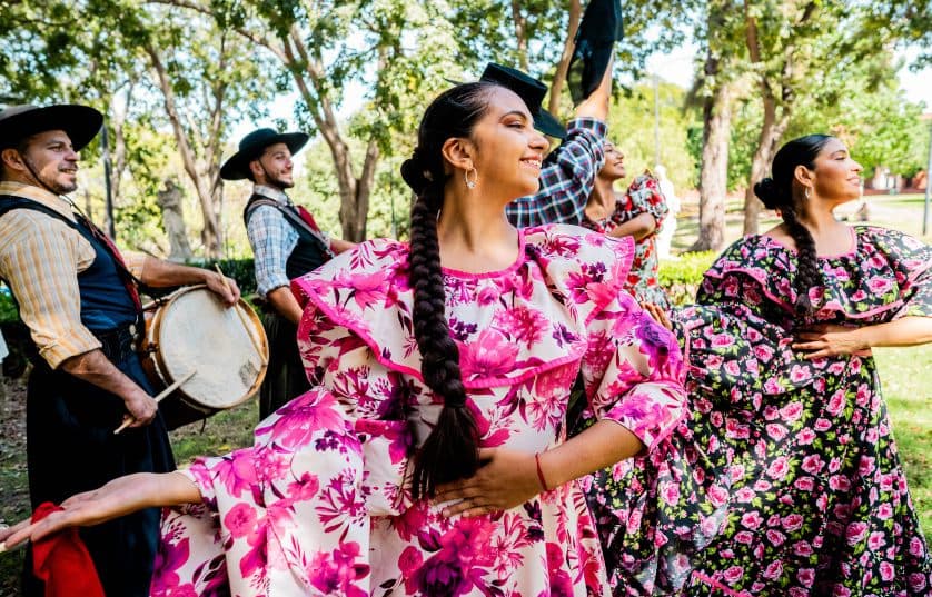 Women in traditional dresses performing a style of dance with men in traditional clothing with drums in background
