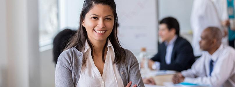 woman smiling with office people in the background sitting around a table