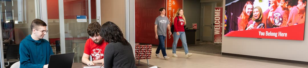 Three students studying at a table with students walking down the hall